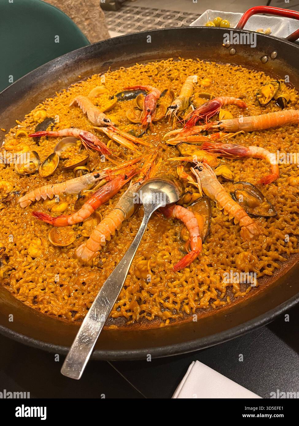 Nahaufnahme einer traditionellen spanischen Paella mit Meeresfrüchten, die in einer Pfanne in Alicante, Spanien, serviert wird. Mit Garnelen, Reis und sattem Safran. - Smartphone-aufgenommenes Stockfoto