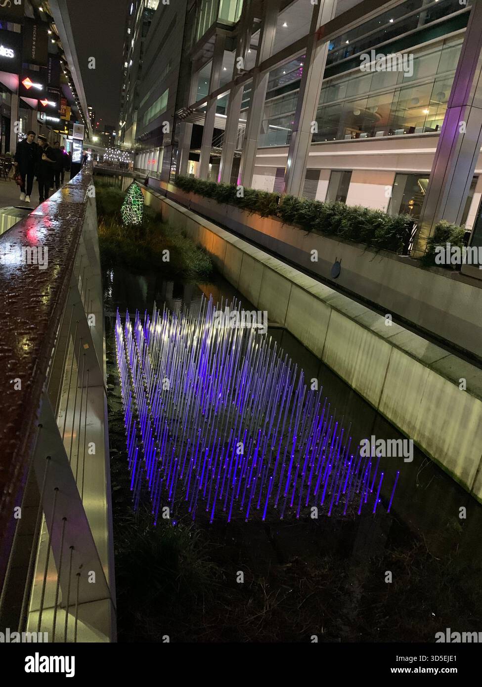 Nachtblick einer modernen beleuchteten Garteninstallation mit leuchtenden lila und blauen Lichtern in einer modernen architektonischen Umgebung in London, England. - Smartphone-aufgenommenes Stockfoto