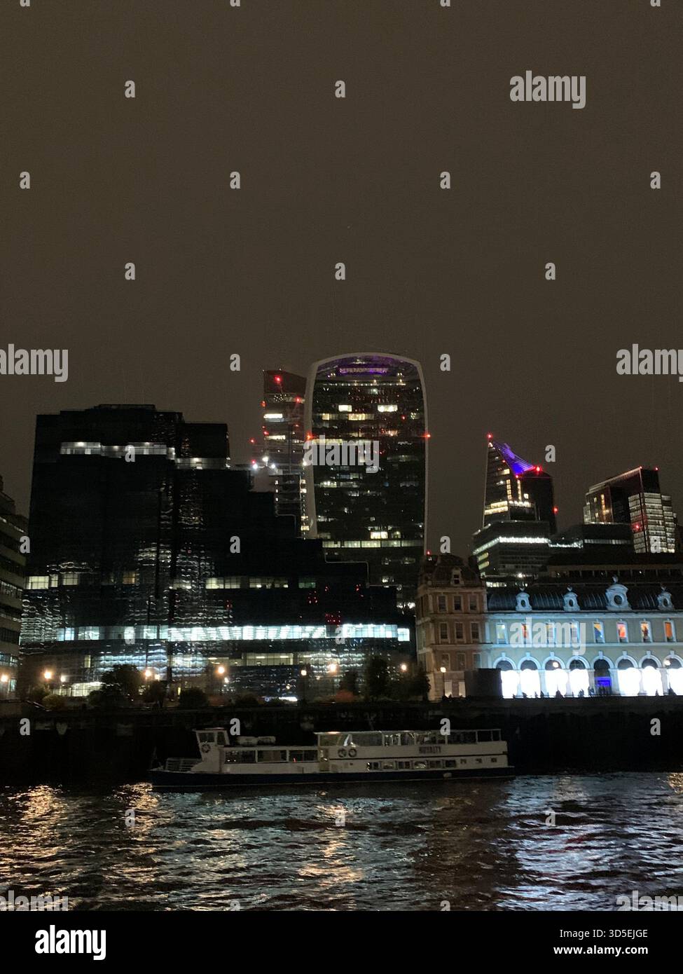 Nächtlicher Blick auf Londons berühmte Tower Bridge, beleuchtet und reflektiert in der Themse. Ein Boot und Details am Fluss - Smartphone-aufgenommenes Stockfoto