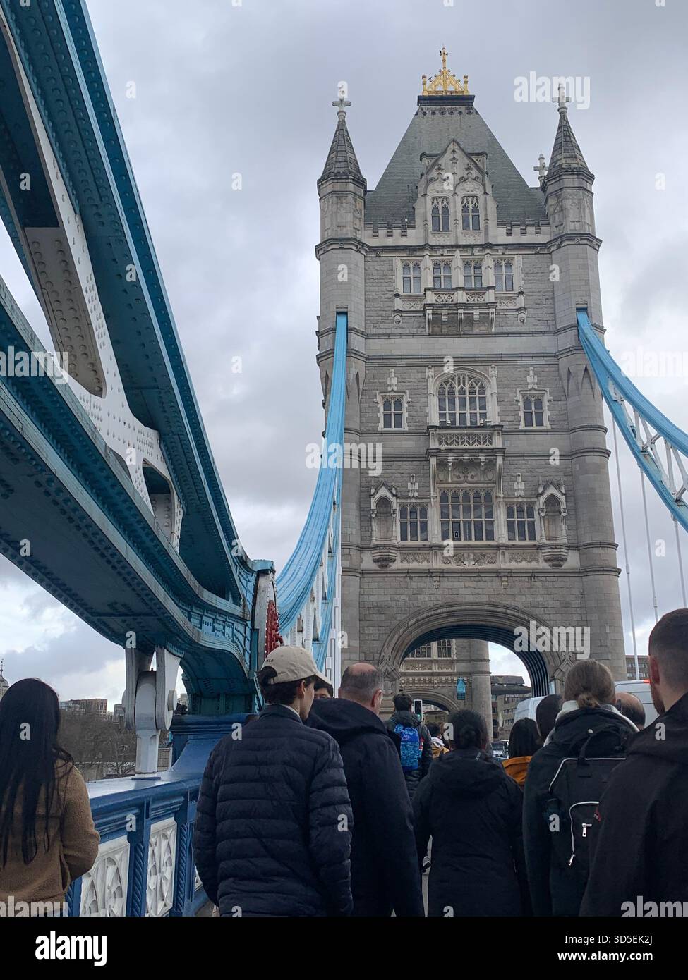Menschen, die über die Tower Bridge gehen, aus nächster Nähe den historischen Steinturm und die blauen Hängelemente sehen. Beliebte Touristenüberquerung in London - Smartphone-aufgenommenes Stockfoto