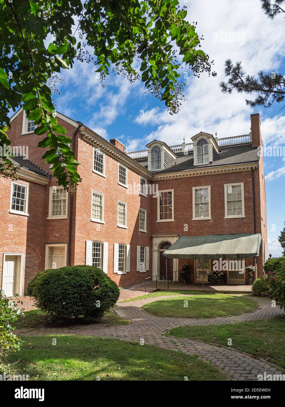 Die Seite des historischen Read House, ein großes rotes Backsteingebäude aus der Kolonialzeit mit weißen Fenstern, eingerahmt von üppig grünem Laub und blauem Himmel in New Castle Stockfoto