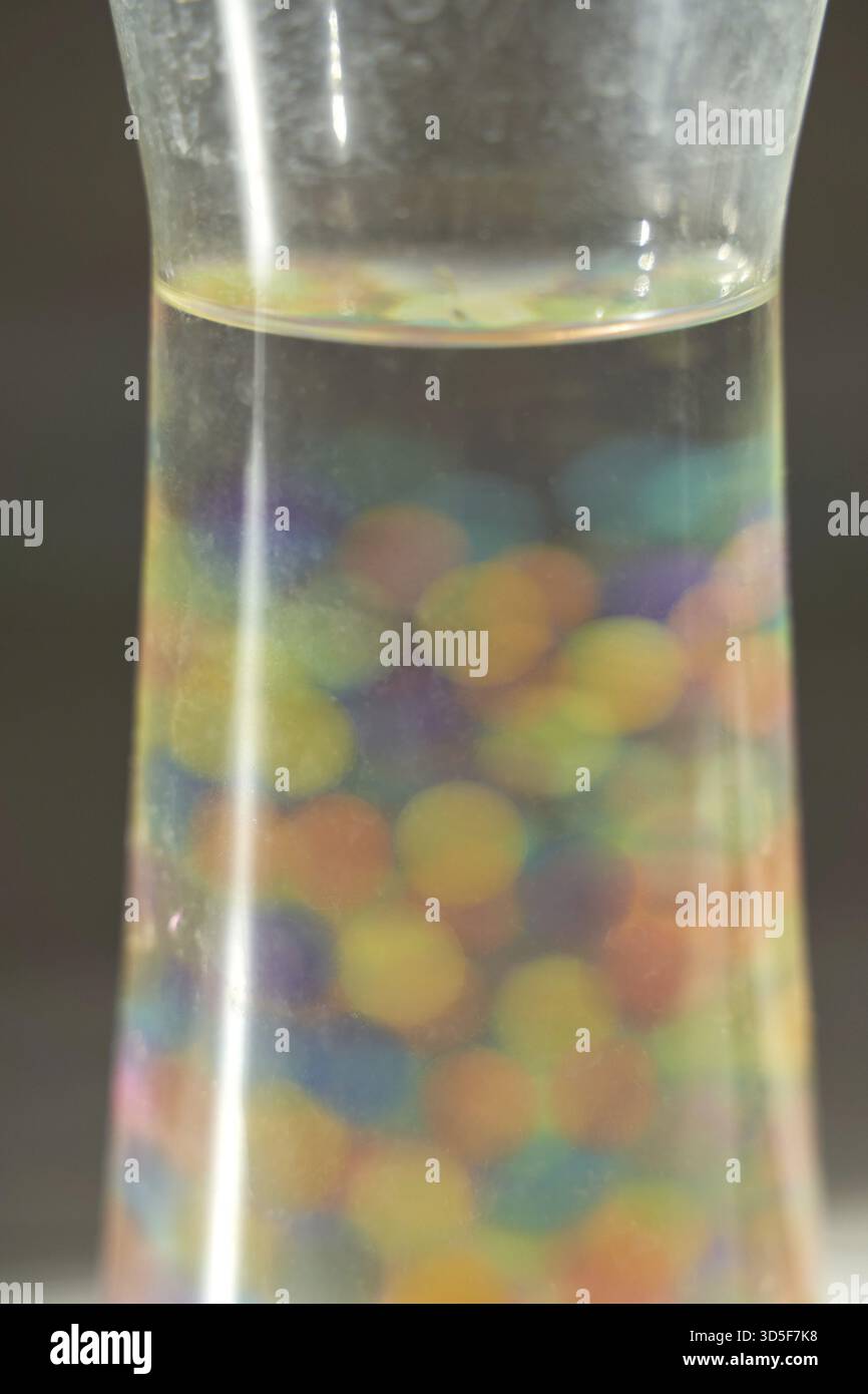 Bunte Wasserperlen, die in einer klaren Flüssigkeit in einem hohen Glasbehälter aufgehängt sind Stockfoto