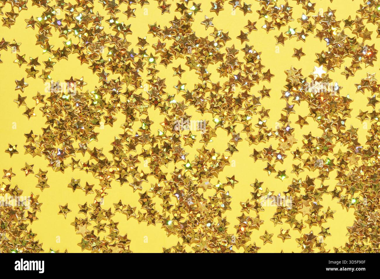 Leuchtendes Goldstern-Konfetti auf gelbem Hintergrund für festliche Feiern und Partydekor Stockfoto