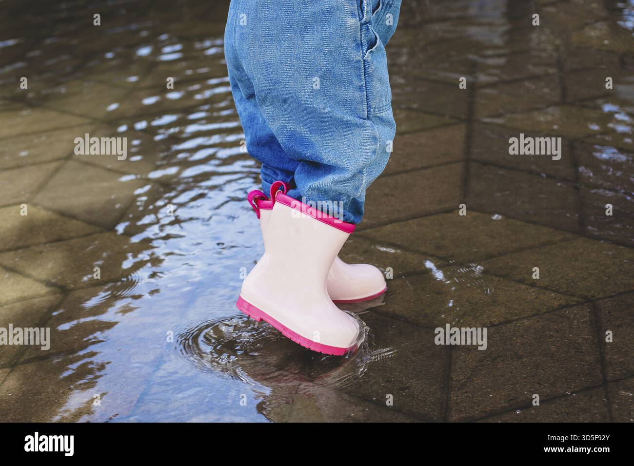 Schließen Sie pinkfarbene Gummistiefel an einem Mädchen in einer Pfütze Stockfoto