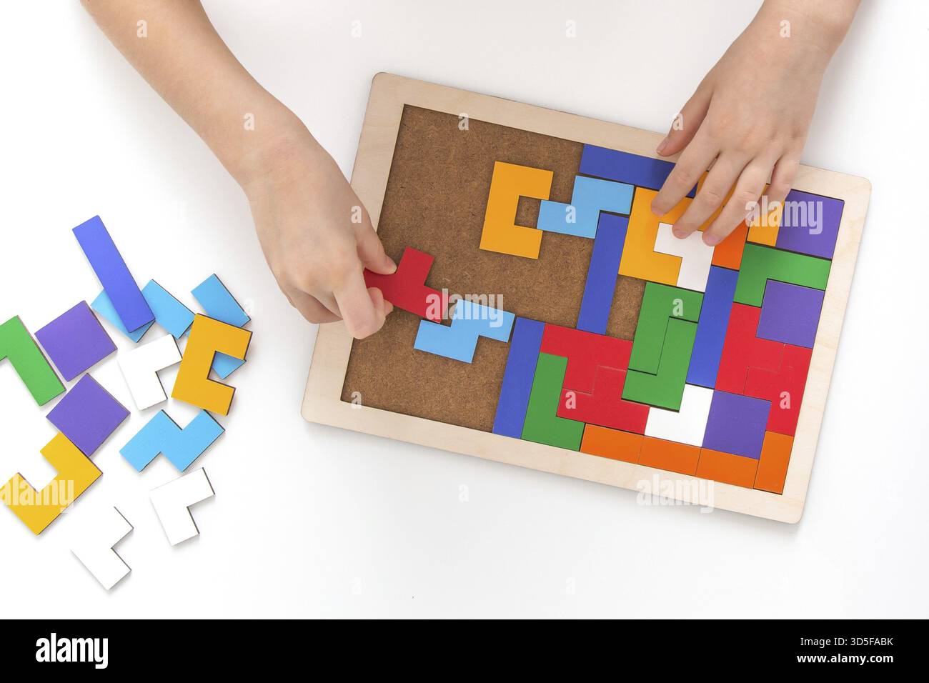 Kinderhände sammeln ein hölzernes mehrfarbiges geometrisches Puzzle auf einem weißen Tisch, das Konzept der Kinderentwicklung und Brettspiele, Blick von oben Stockfoto