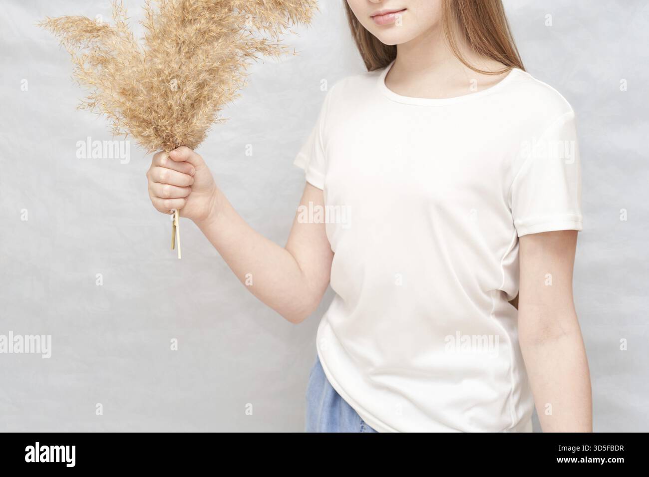 Junge kaukasische Frau mit getrocknetem Pampasgras in lässigem weißem T-Shirt Stockfoto