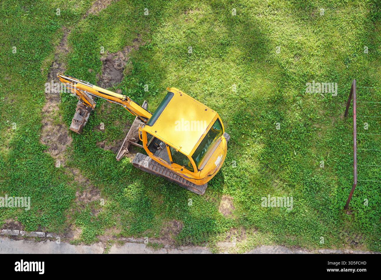 Kleiner Bagger, auf grünem Gras geparkt, aus der Vogelperspektive Stockfoto