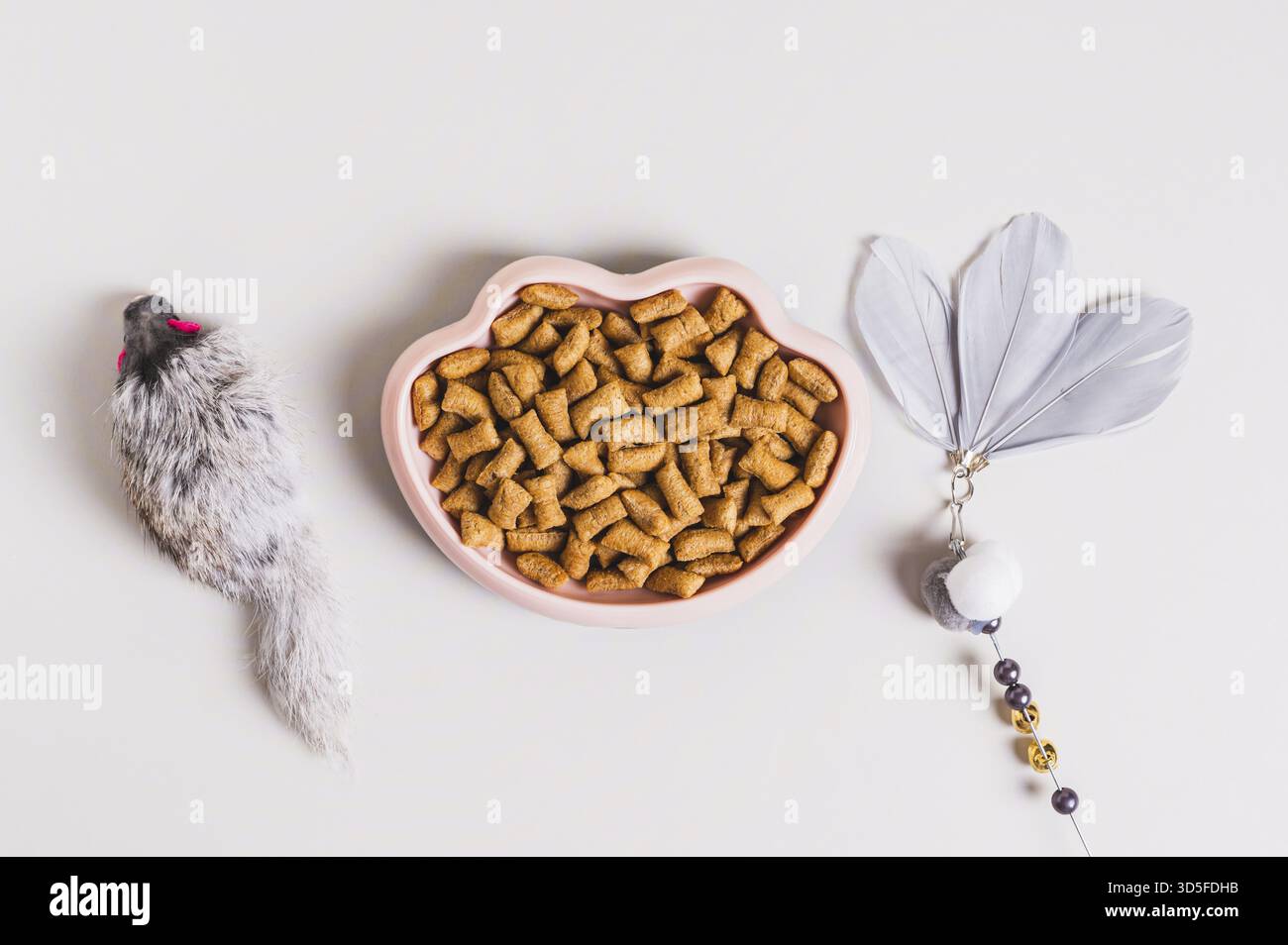 Schüssel mit trockenem Katzenfutter und Spielzeug auf dem Tisch Stockfoto