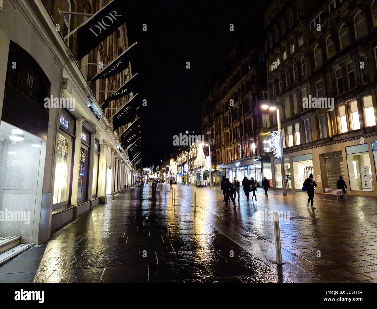 Straßenbild einer Einkaufsstraße, Buchanan Street in Glasgow, Schottland. Die Leute laufen nachts auf der Straße entlang. Lichter, die auf nasser Oberfläche reflektiert werden Stockfoto