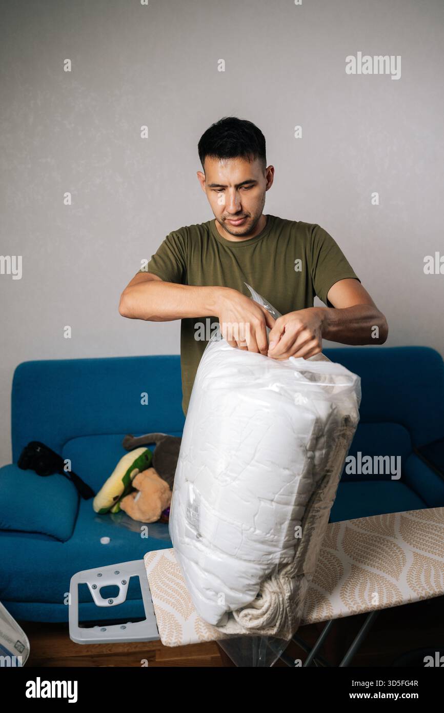 Vertikales Porträt eines jungen Mannes, der einen großen, transparenten Staubeutel mit weißer Bettwäsche schließt, mit doppeltem Reißverschluss, um luftdicht zu machen Stockfoto