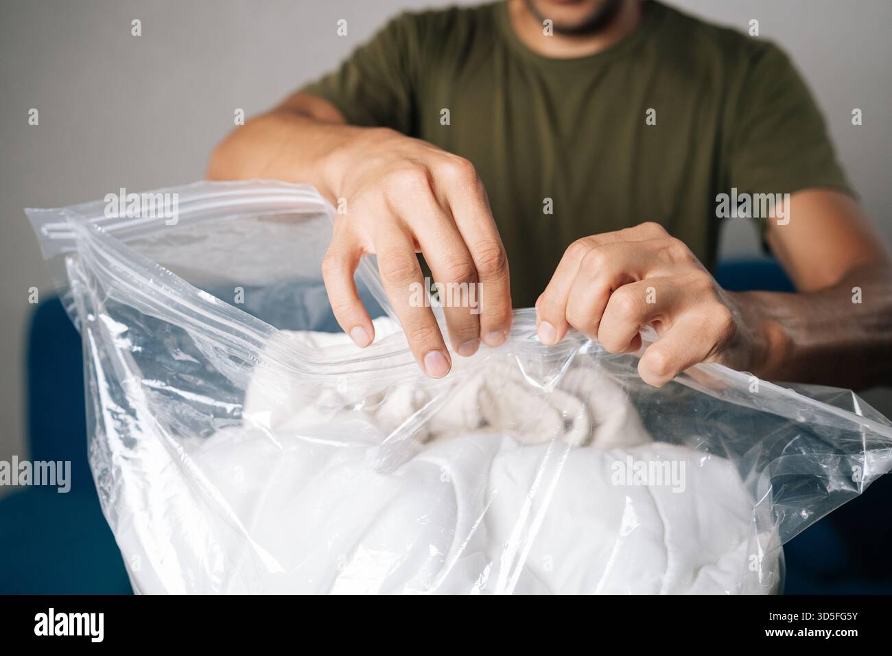 Nahaufnahme männlicher Hände, die große transparente Vakuumtasche mit weißer Bettwäsche schließen, mit doppeltem Reißverschluss für luftdichte Abdichtung Stockfoto