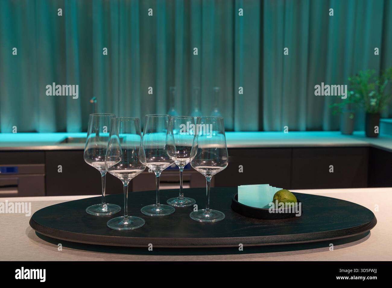 . Elegante Weingläser sind ordentlich auf einem dunklen Tablett angeordnet, ergänzt durch grüne Umgebungsbeleuchtung und eine Limette, die eine elegante Atmosphäre schafft Stockfoto