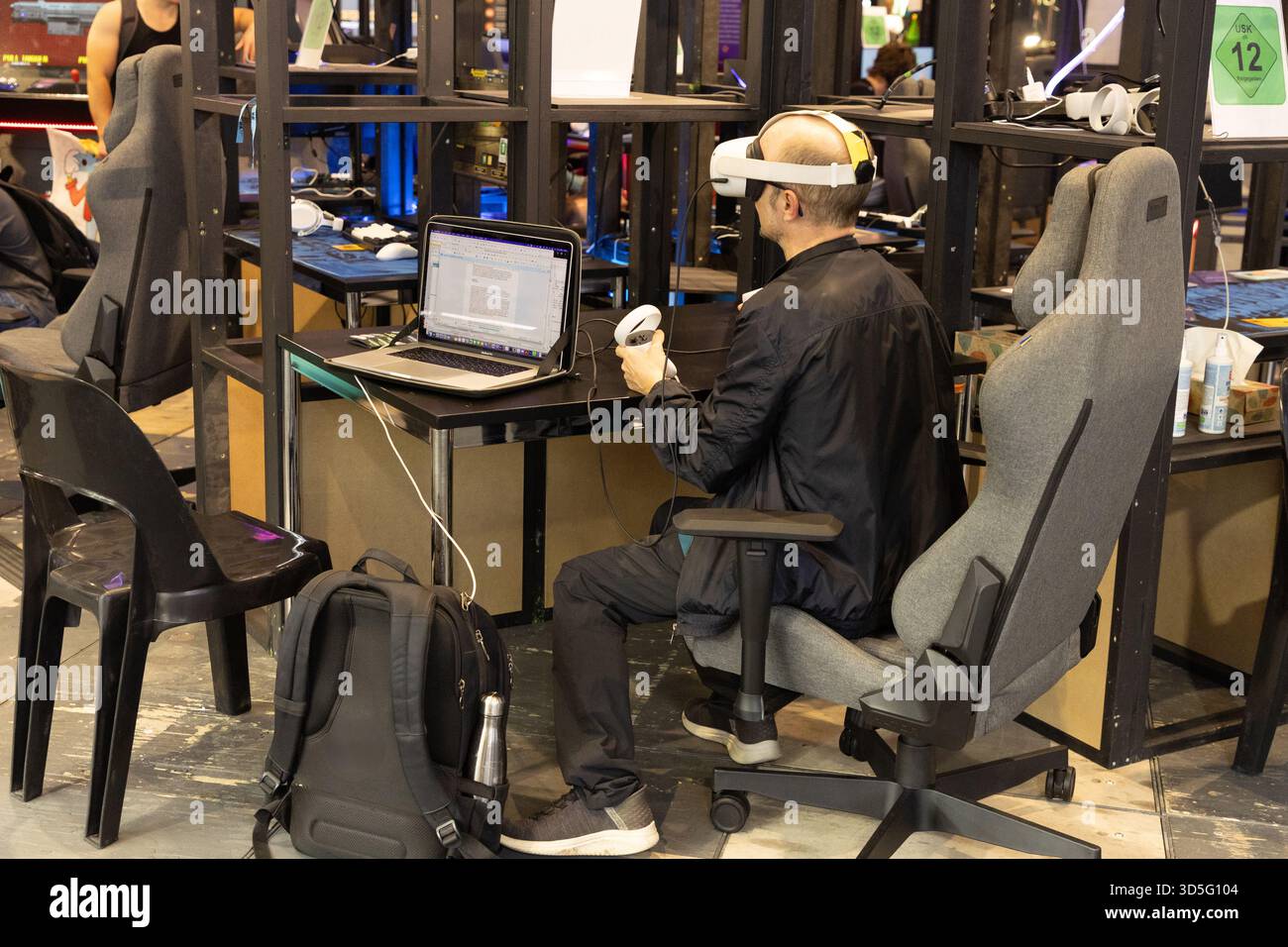 Berlin, Deutschland - 09. September 2025: IFA.Berlin. Mann mit Virtual-Reality-Headset arbeitet an einem modernen Schreibtisch mit Laptop Stockfoto