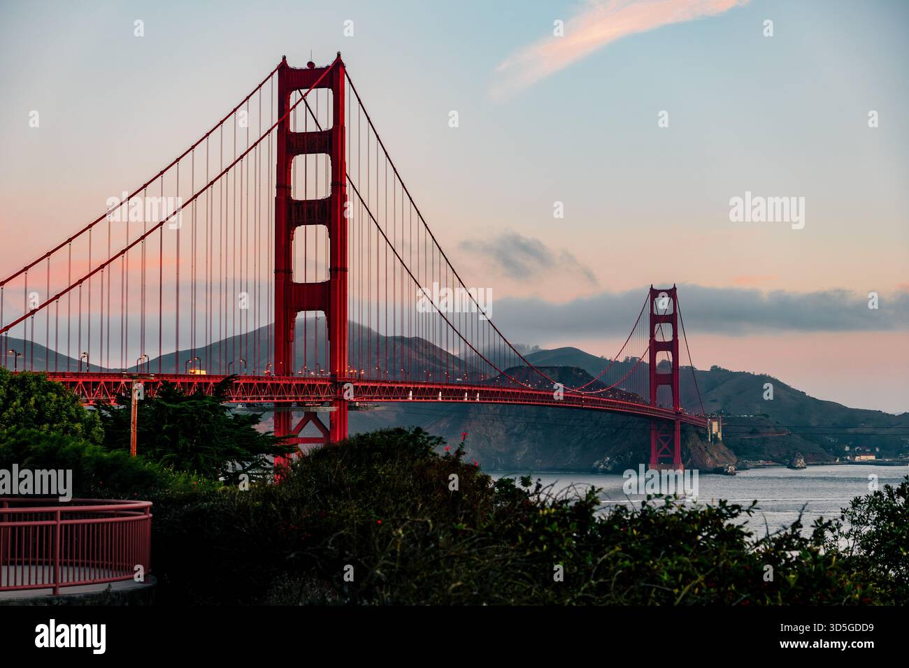 Die legendäre Golden Gate Bridge steht majestätisch vor einem weichen Dämmerhimmel, dessen charakteristischer roter Farbton über der Bucht von San Francisco herausragt. Stockfoto