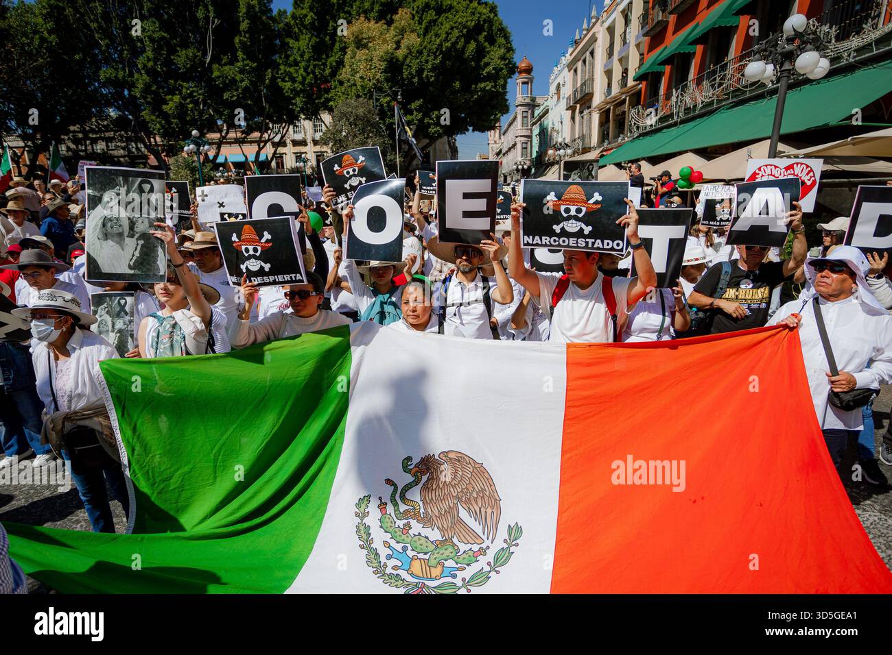 Die Demonstranten in Puebla halten die mexikanische Flagge, während sie Schilder hissen, die „NARCOESTADO“ (Narco-Staat) buchstabieren, und äußern starke Kritik an der Regierung Stockfoto