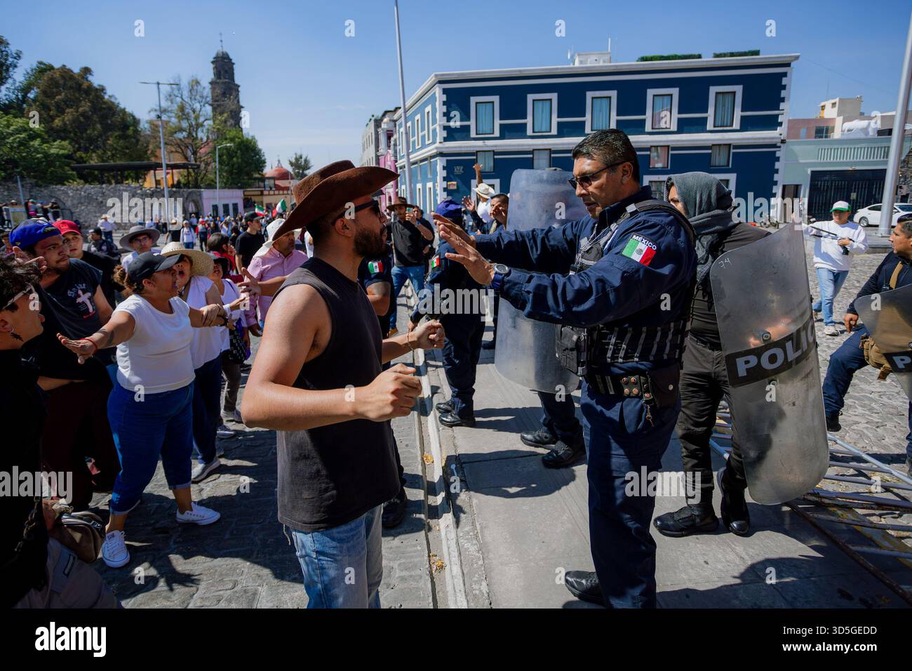 Ein Demonstrant mit Hut konfrontiert einen Polizisten während des demonstrationsmarsches auf den Straßen des historischen Zentrums von Puebla, Mexiko. Stockfoto