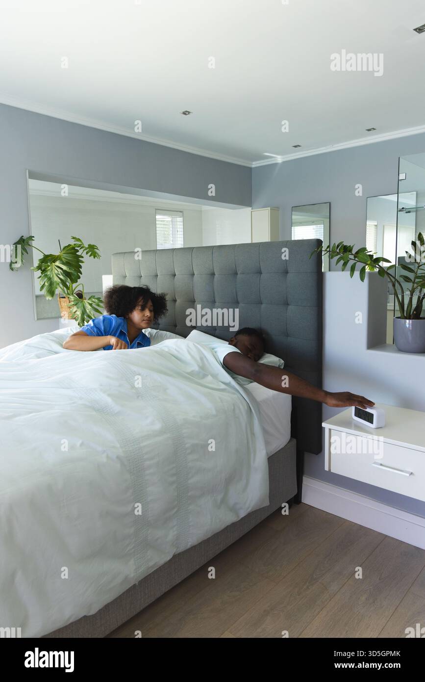 Junges Paar, das in einem modernen Schlafzimmer aufwacht und den Wecker auf dem Nachttisch in der Nähe des Arms ansieht Stockfoto