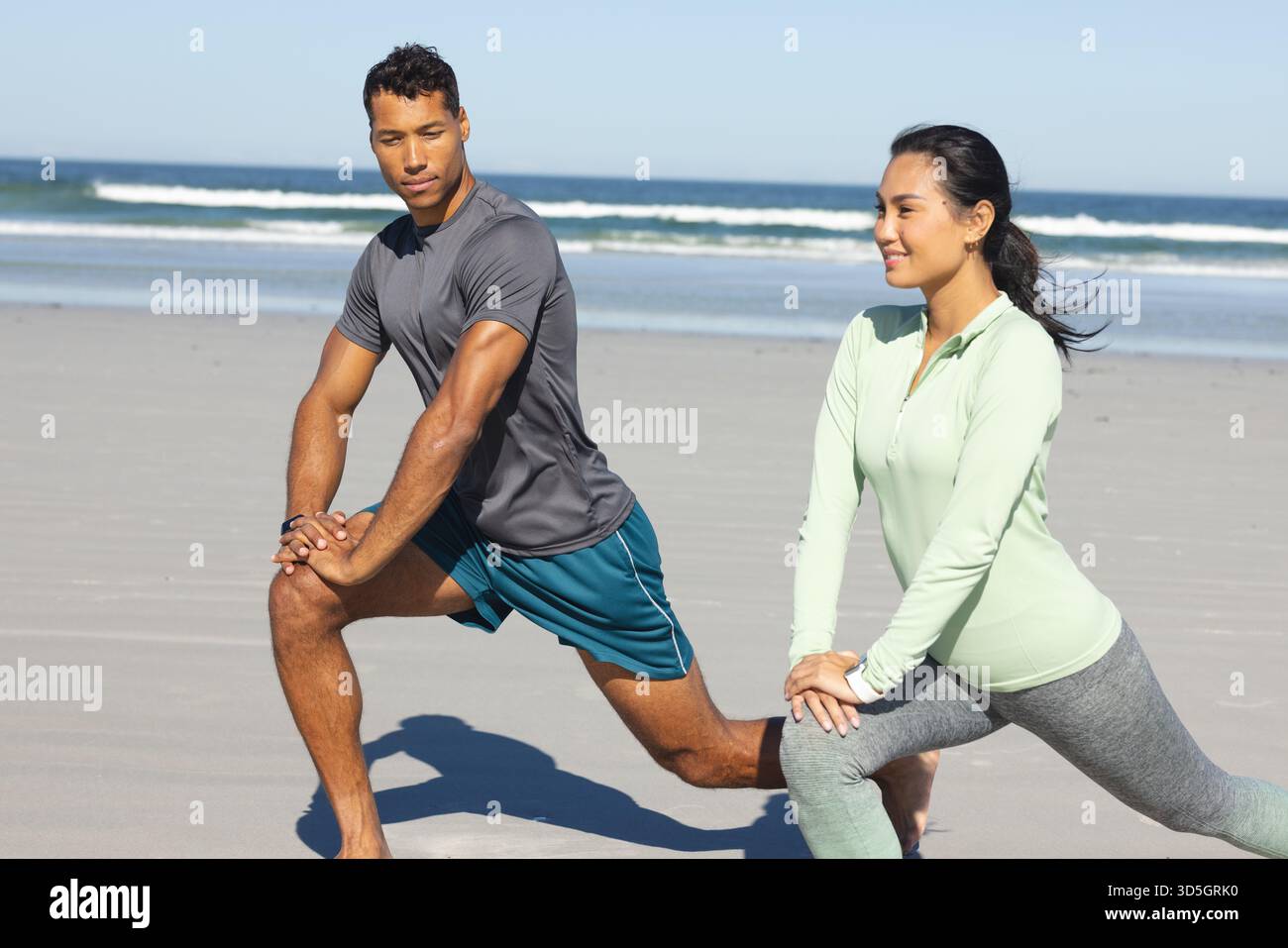 Paare trainieren am Strand, Strecken Beine und genießen sonniges Workout am Morgen Stockfoto