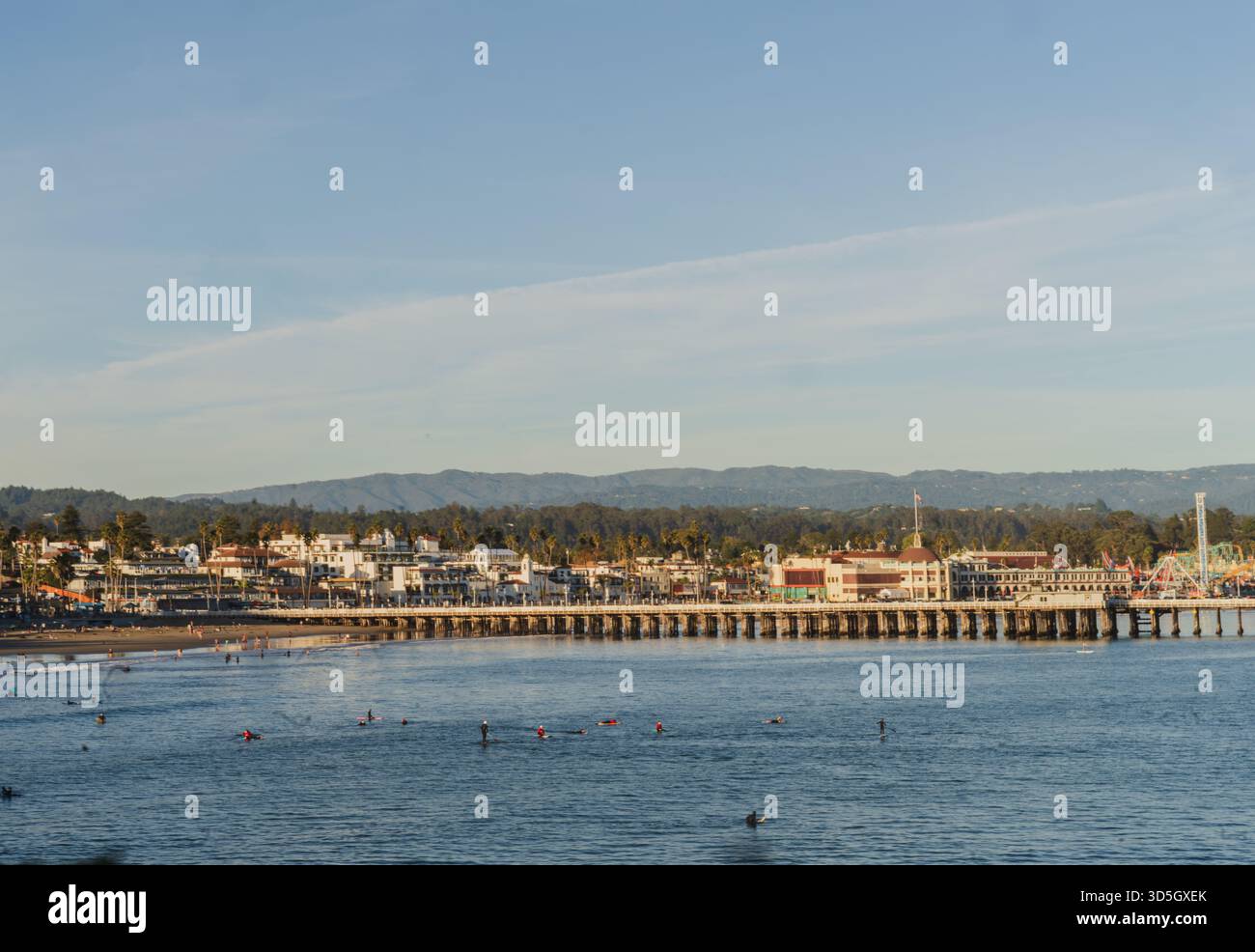 Ein Blick auf den Santa Cruz Pier und die Promenade am frühen Sonnenuntergang, während Surfer auf Wellen im Pazifischen Ozean warten. Stockfoto
