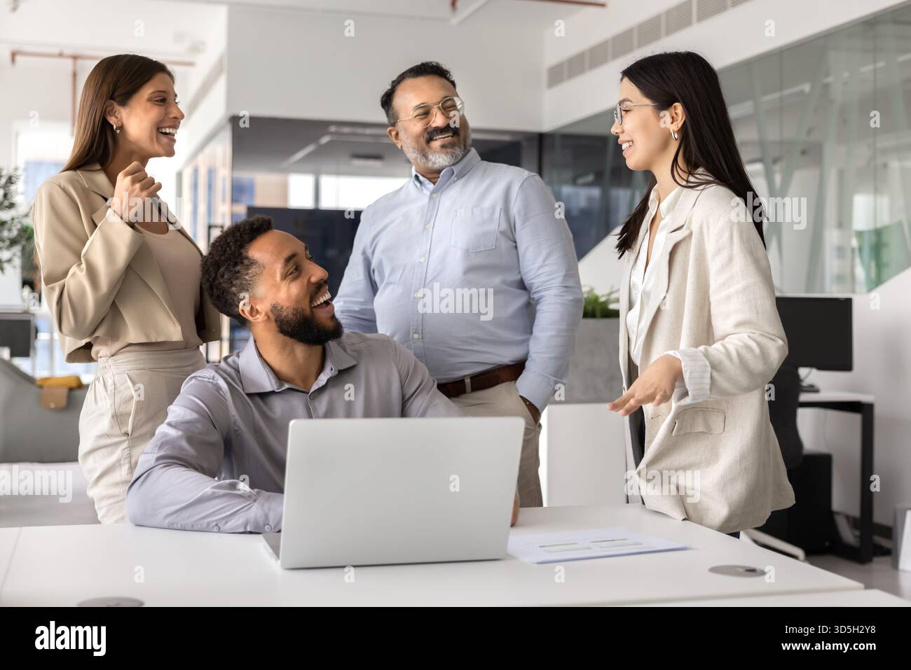 Glückliche Kollegen, die am Arbeitsplatz zusammen stehen und sitzen Stockfoto