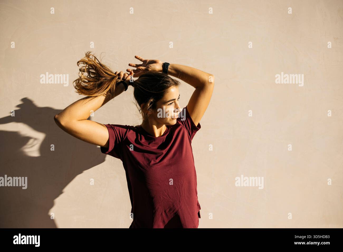Eine Frau, die draußen steht und ihren Pferdeschwanz fesselt und sich auf ein Training vorbereitet Stockfoto