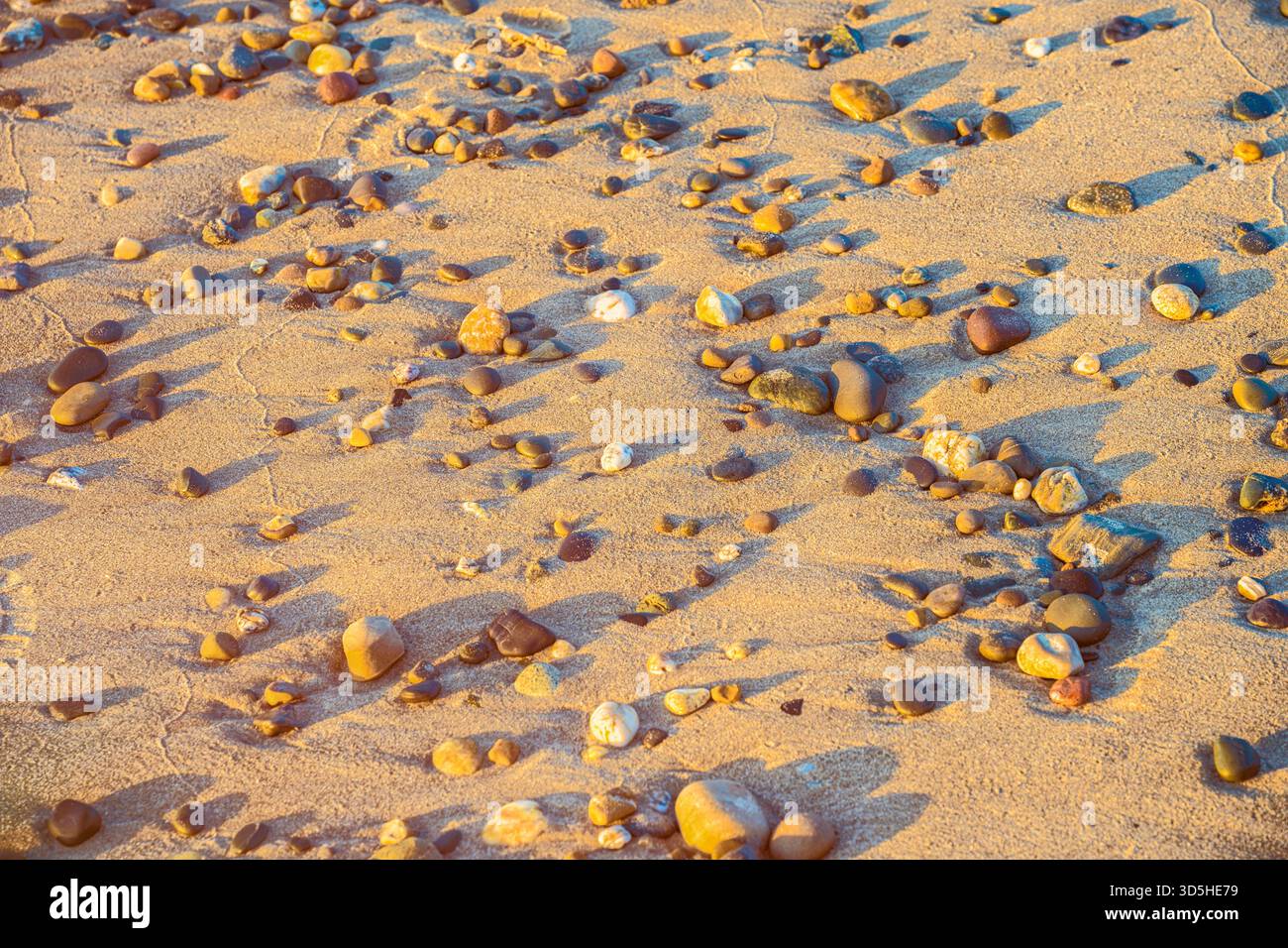 Herbstnachtgleiche-Makro aus bunten Kieselsteinen am irischen Strand mit Sandkräuseln und natürlichen Mustern Stockfoto
