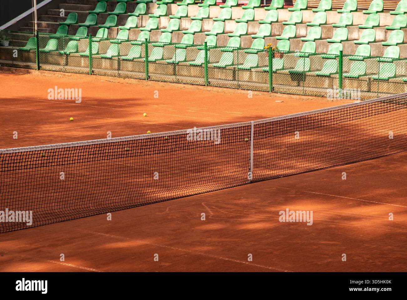 Das Tennisnetz erstreckt sich über einen ruhigen Lehmplatz und schafft eine minimale Sportszene, die sich auf Form und Atmosphäre konzentriert Stockfoto