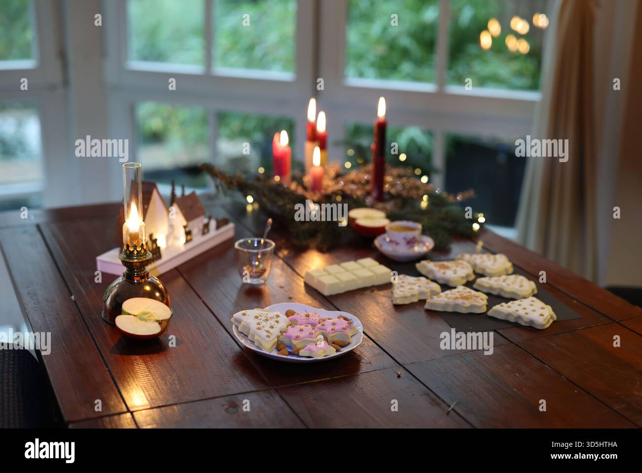 Hausgemachte Weihnachtsplätzchen auf einem rustikalen Holztisch mit Kerzen, Orangen und festlicher Winterdekoration. Stockfoto
