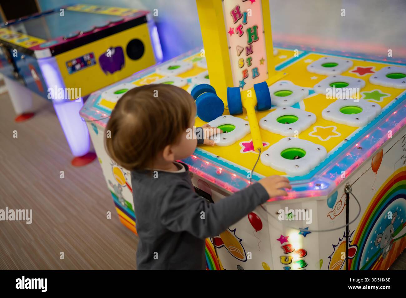 Ein Kind interagiert mit einem lebhaften Arcade-Spiel mit Lichtern, Löchern und verspielten Grafiken in einer familienfreundlichen Innenumgebung Stockfoto