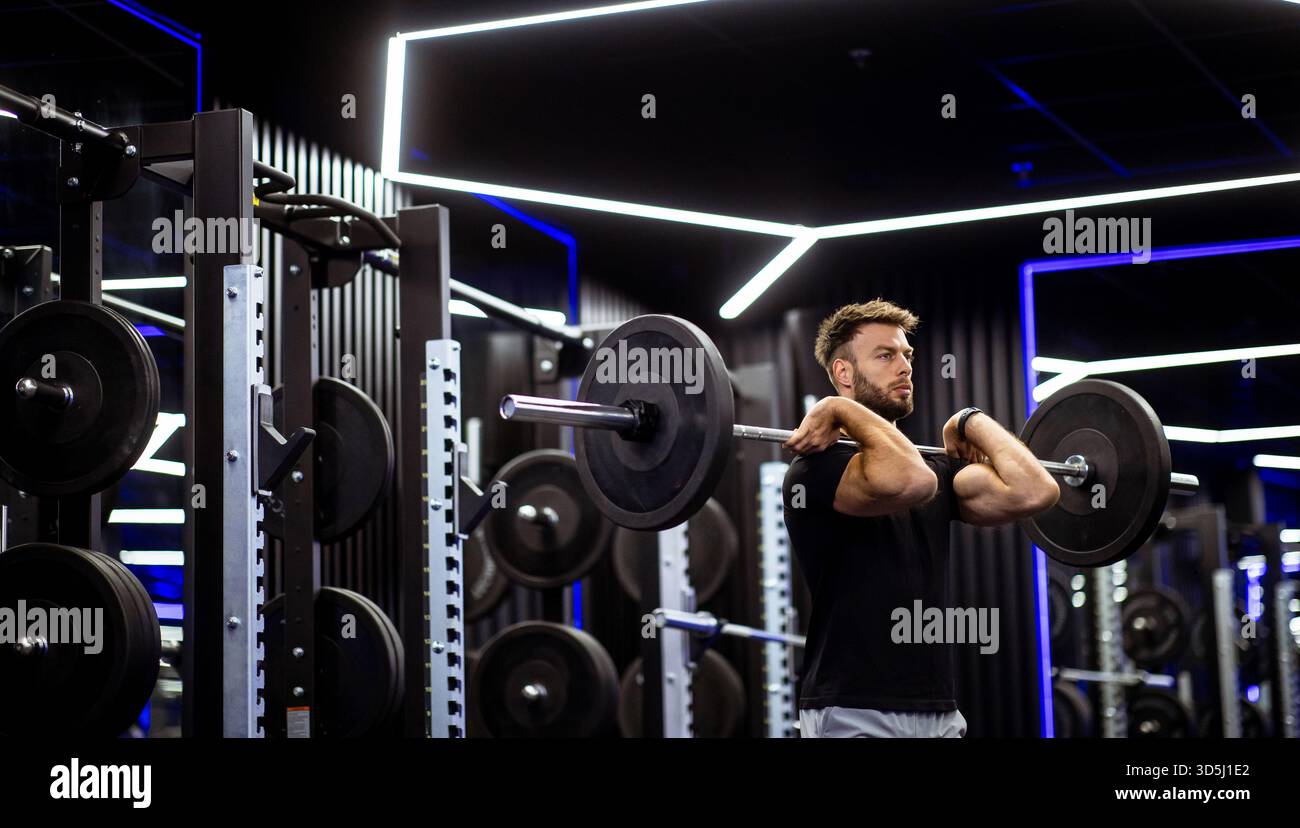 Ein Mann führt einen Langhantellift in einem stilvollen Fitnessstudio, umgeben von Fitnessgeräten und dynamischer Beleuchtung. Er konzentriert sich auf die Aufrechterhaltung der richtigen Form A Stockfoto