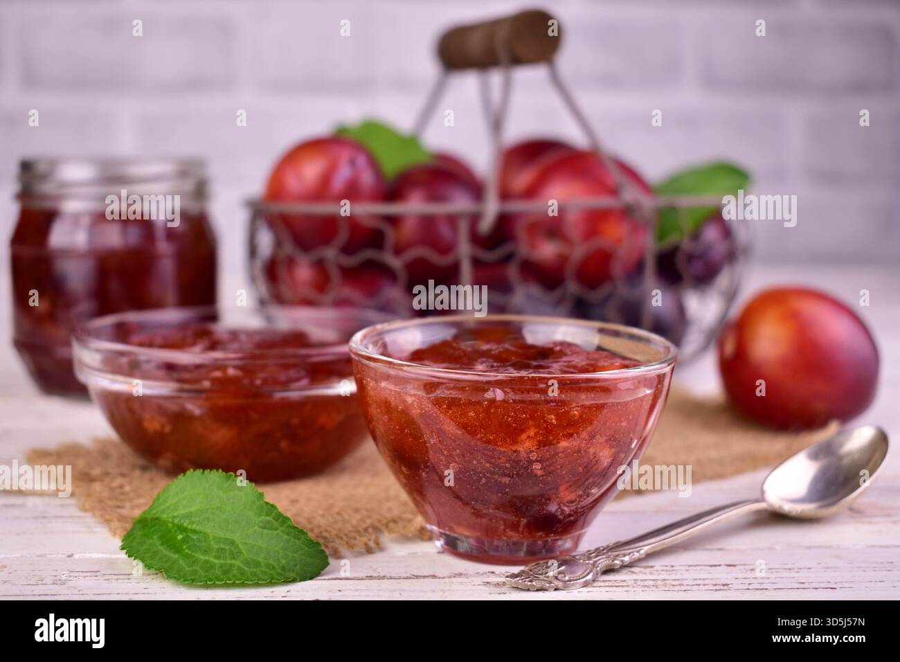 Hausgemachte Pflaumenmarmelade in einer Glasschale vor dem Hintergrund frischer Pflaumen. Stockfoto