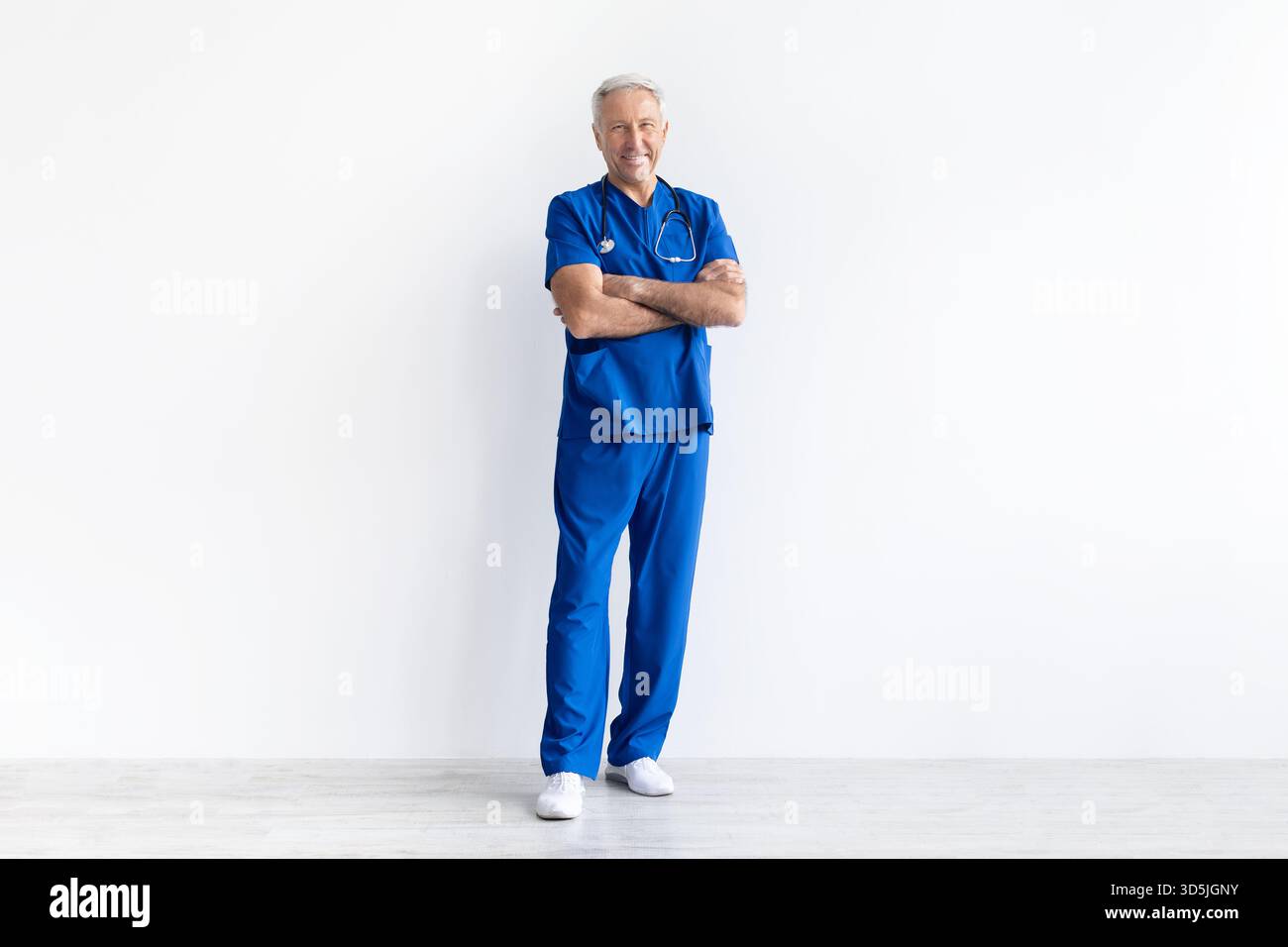 Leitender männlicher Arzt in Uniform stehend mit überkreuzten Armen auf weißem Hintergrund Stockfoto