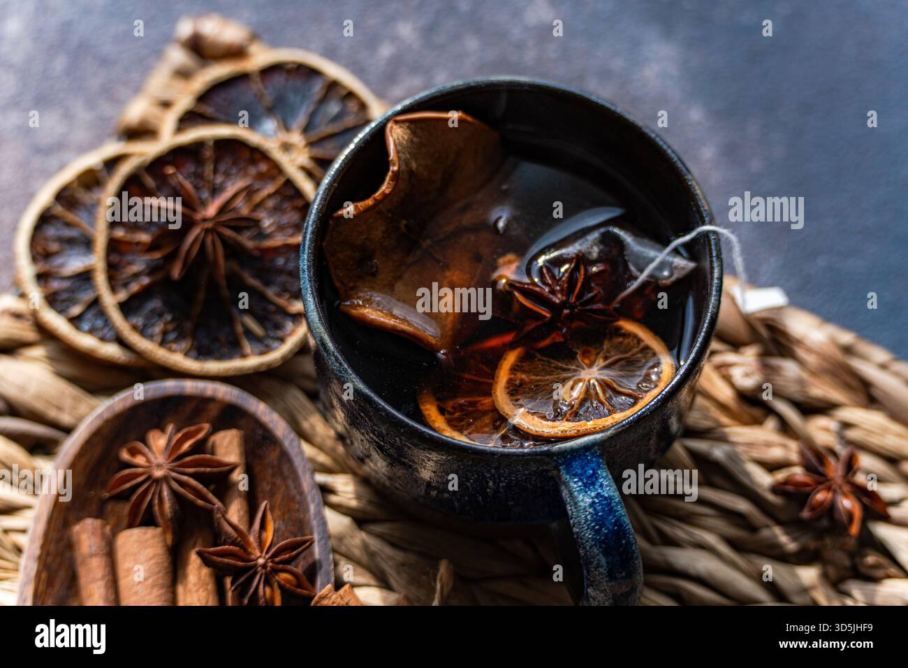Nahaufnahme einer Tasse Glühtee mit verschiedenen Gewürzen auf einer rustikalen Tischmatte Stockfoto