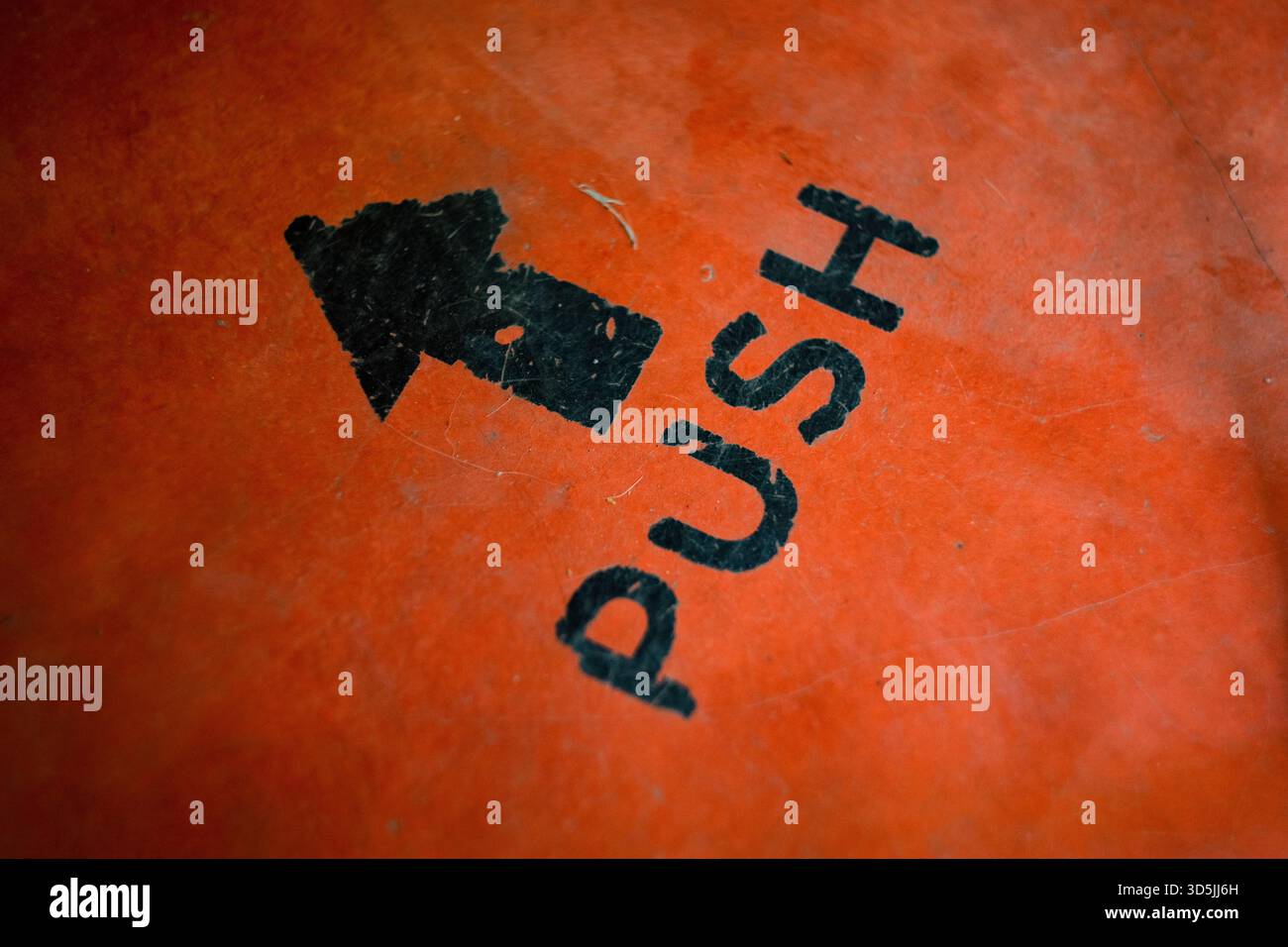 Nahaufnahme von schwarzem „PUSH“-Text und Pfeil auf orangefarbener Oberfläche Stockfoto