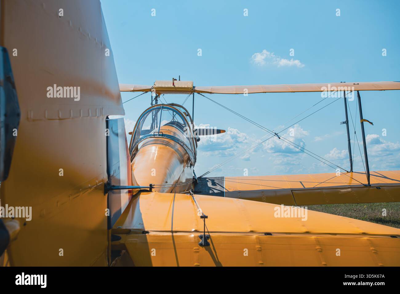 Vorderansicht des zweiflügeligen Vintage-Gelbflügels mit offenem Cockpit, oberen und unteren Flügeln, Stützstreben und Drahtantrieb auf der Start- und Landebahn. Klarer blauer Himmel mit Stockfoto