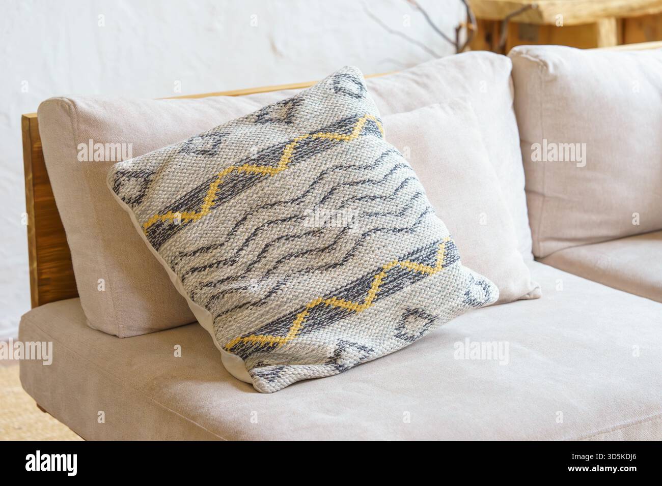 Weiches Dekokissen, Kissen mit geometrischer Webstruktur und gelbem Zickzackmuster auf hellbeigem Sofa. Gemütliches, minimalistisches skandinavisches Interieur mit Stockfoto