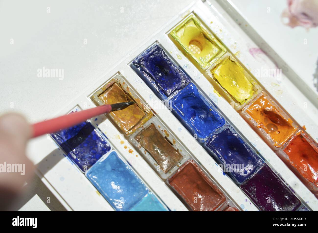Farbenfrohe Aquarellpalette mit hellen Pigmenten und Pinsel für künstlerische Ausdrucksformen Stockfoto