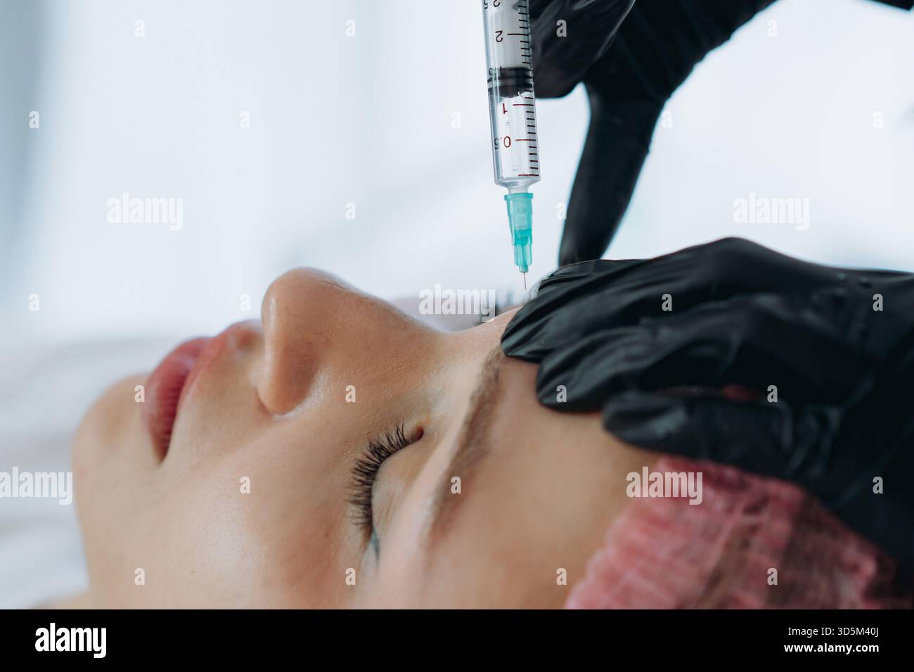 Nahaufnahme von professionellen Händen, die eine Verjüngungsinjektion in die Stirnfalte der Frau machen Stockfoto