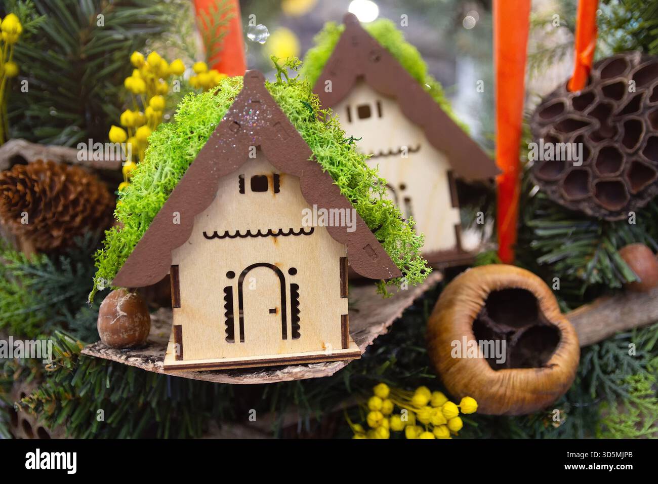 Ein bezauberndes hölzernes Miniaturhaus hängt an einem Weihnachtsbaum. Weihnachtsdekoration Stockfoto