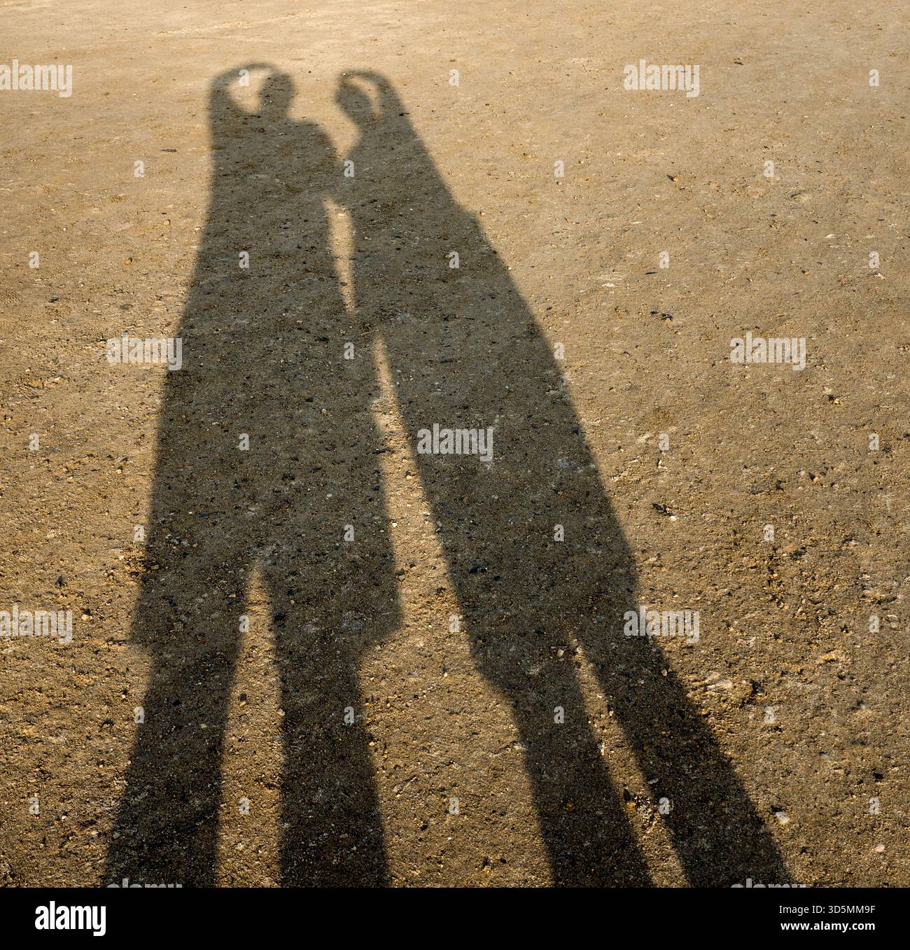 Zwei Silhouetten werfen Schatten in den Sand, während sie das OK-Handsignal des Tauchers bilden und einen verspielten und ausdrucksstarken Strandmoment erzeugen Stockfoto