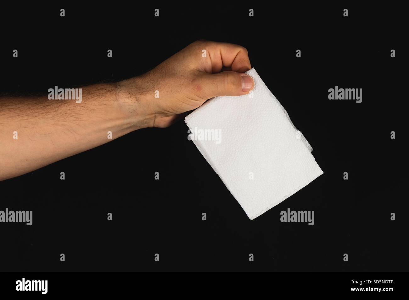 Eine Hand greift einen Stapel sauberer, weißer Papiertücher vor einem schwarzen Hintergrund. Die Szene unterstreicht die Einfachheit und den Nutzen des Alltags Stockfoto