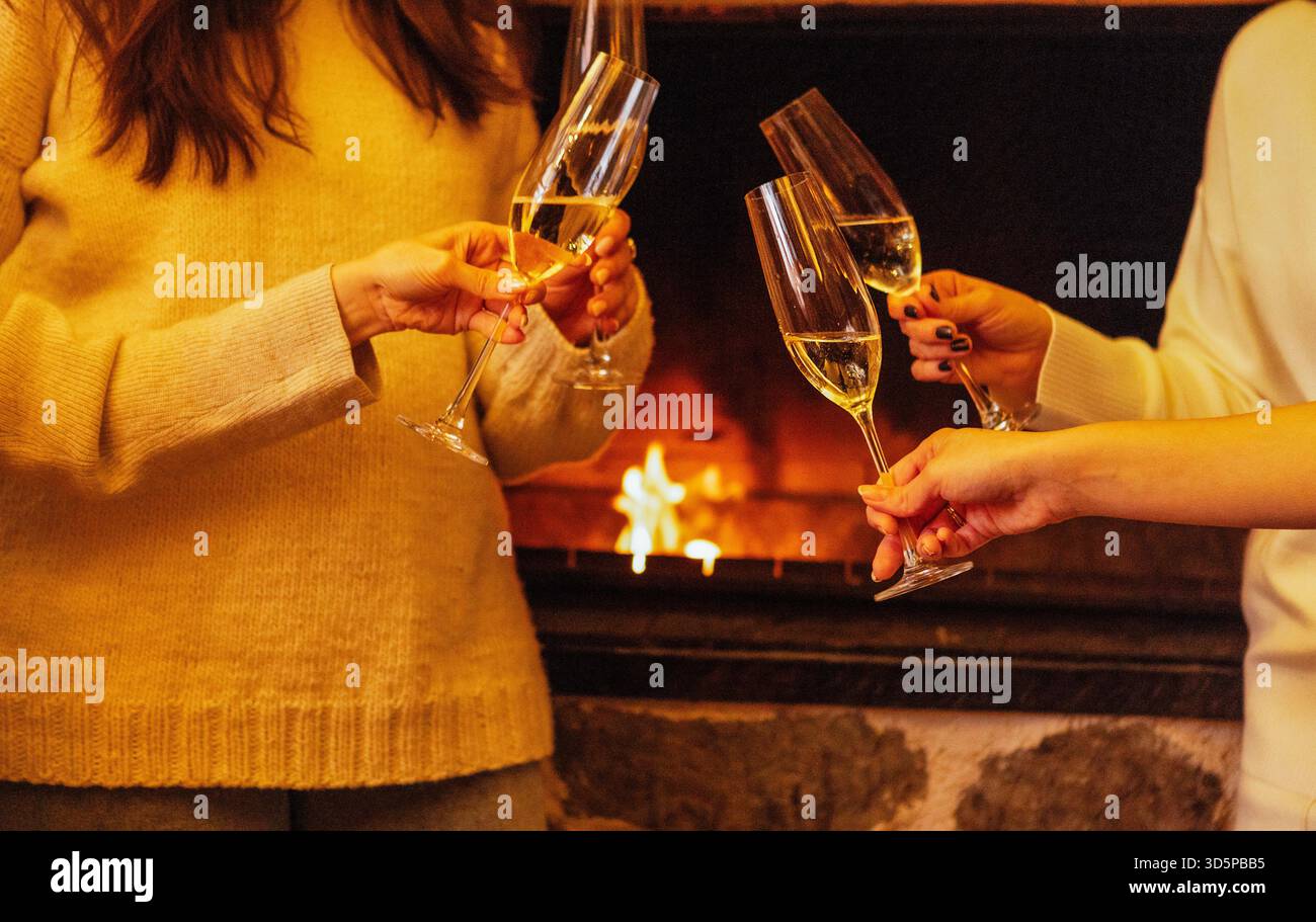 Frauen toasten mit Sektgläsern vor einem warmen Kamin und schaffen ein gemütliches Ambiente, das während einer festlichen Okka mit Freude und Feier erfüllt ist Stockfoto