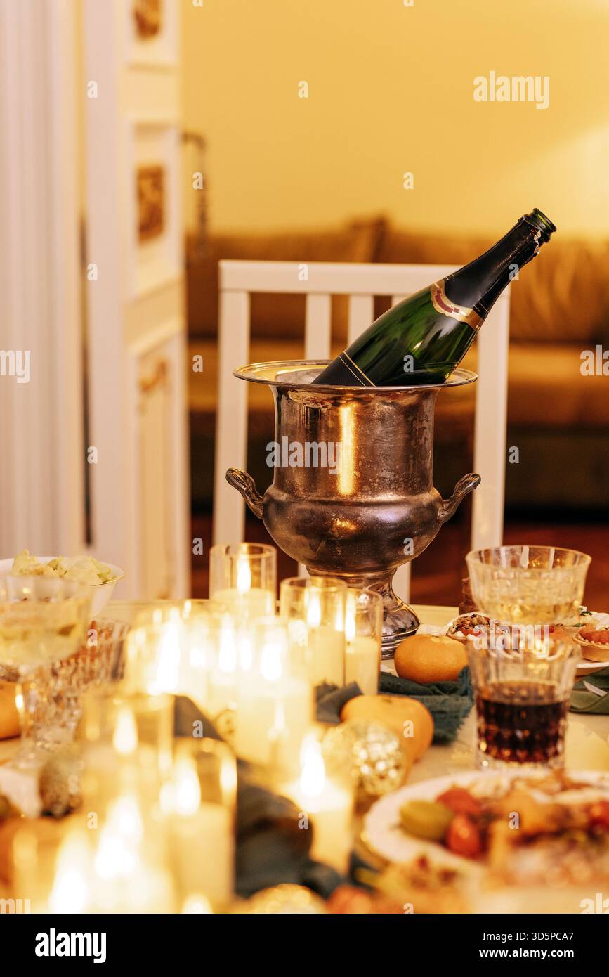 Wunderschön gestalteter Esstisch für Feiern, mit Champagner im Eiskübel, umgeben von Kerzen und köstlichen Desserts, sorgt für ein festliches fest Stockfoto