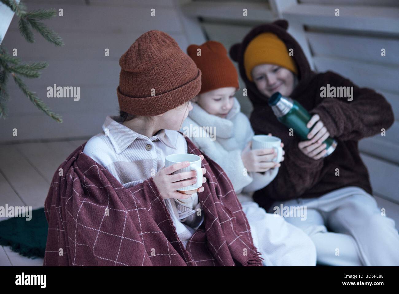 Gruppe von Kindern in Winterkleidung, sitzen drinnen und teilen warme Getränke, schaffen ein gemütliches Ambiente mit weichen Texturen und festlicher Atmosphäre Stockfoto