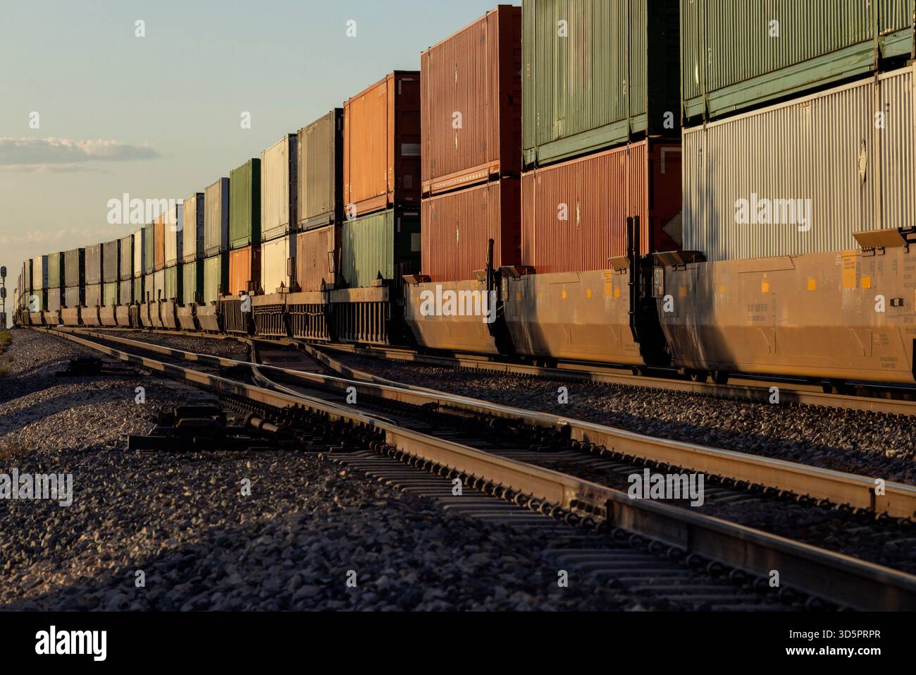 Ein langer Containerzug, der bei Sonnenuntergang vorbeifährt Stockfoto