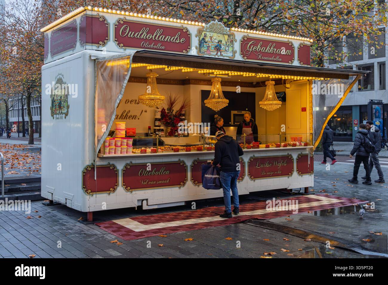 Ein wunderschön beleuchteter „Oudhollandse Oliebollen Gebakkraam“ (traditioneller niederländischer Konditorstand) auf einem Rotterdamer Platz, auf dem Winterspezialitäten serviert werden. Rotterda Stockfoto