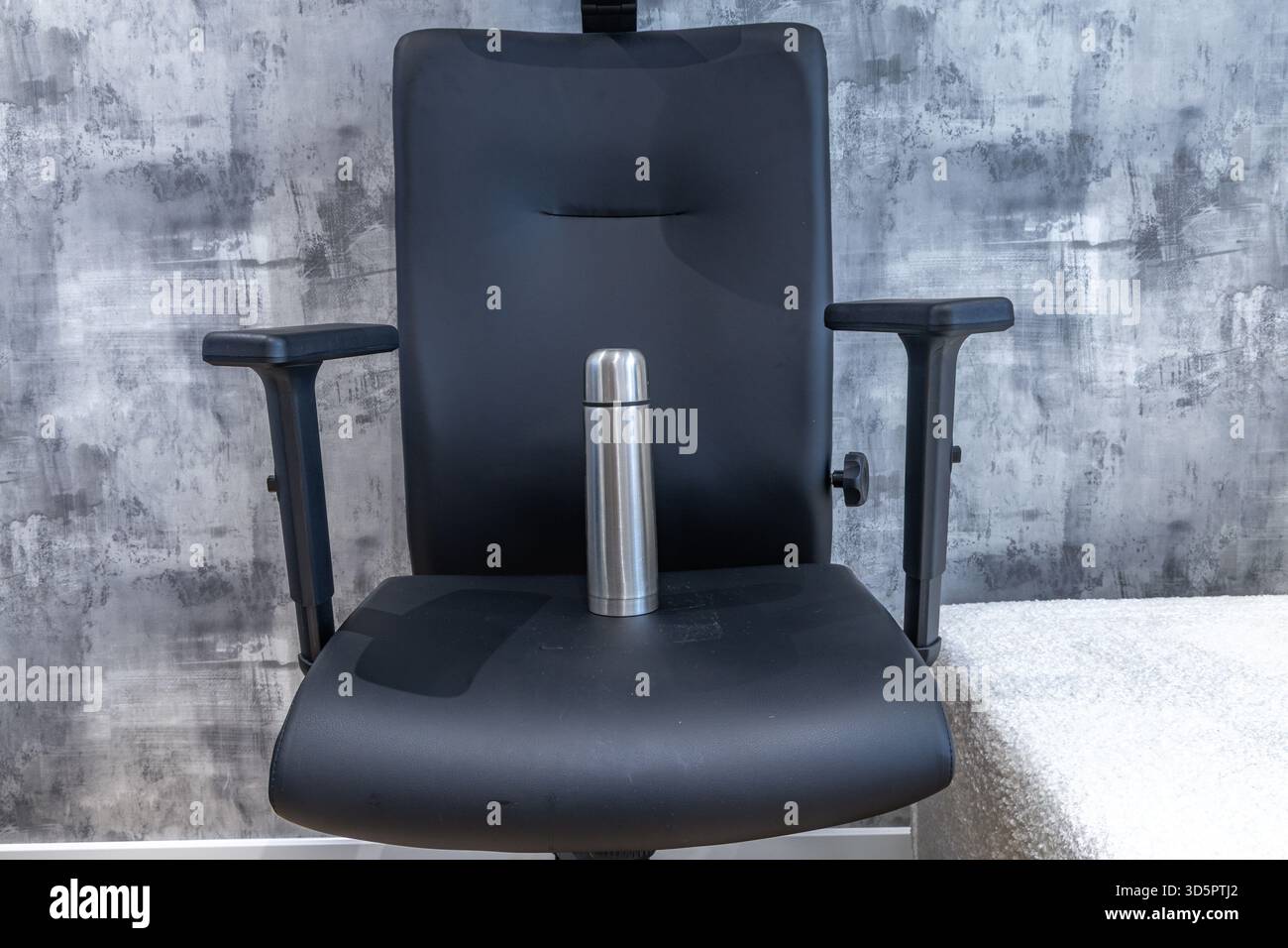 Eine Thermoskanne für heiße Getränke sitzt auf einem Lederdrehstuhl im Büro. Stockfoto