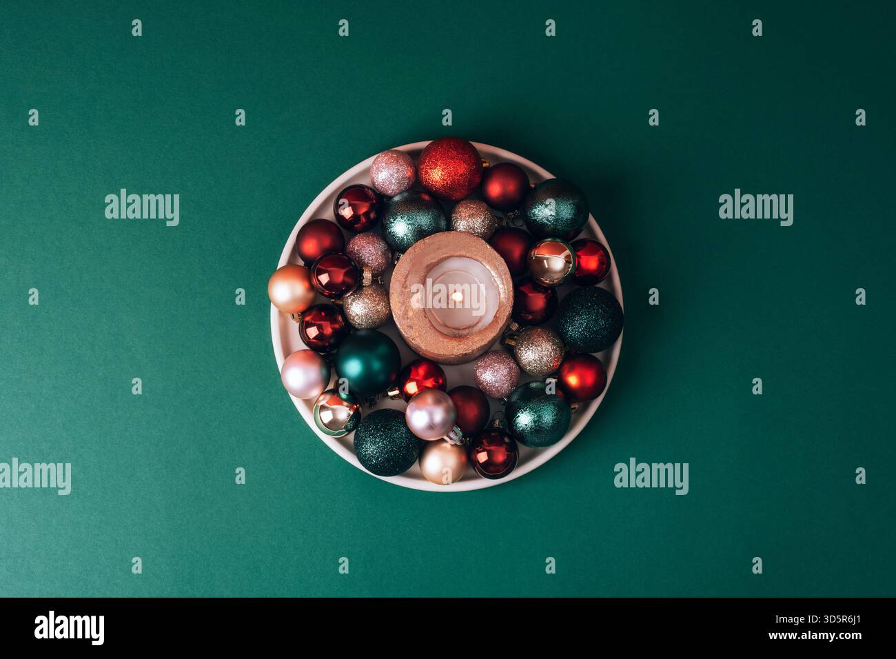 Kerze mit Weihnachtsschmuck in der Schüssel auf dunkelgrünem Hintergrund. Draufsicht, flach. Stockfoto