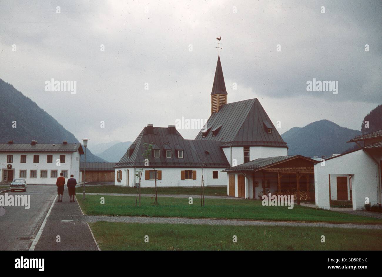 Zwei Frauen gehen an einer Kirche auf dem Bürgersteig vorbei. Ein Auto steht auf der Straße. [Automatisierte Übersetzung] Stockfoto