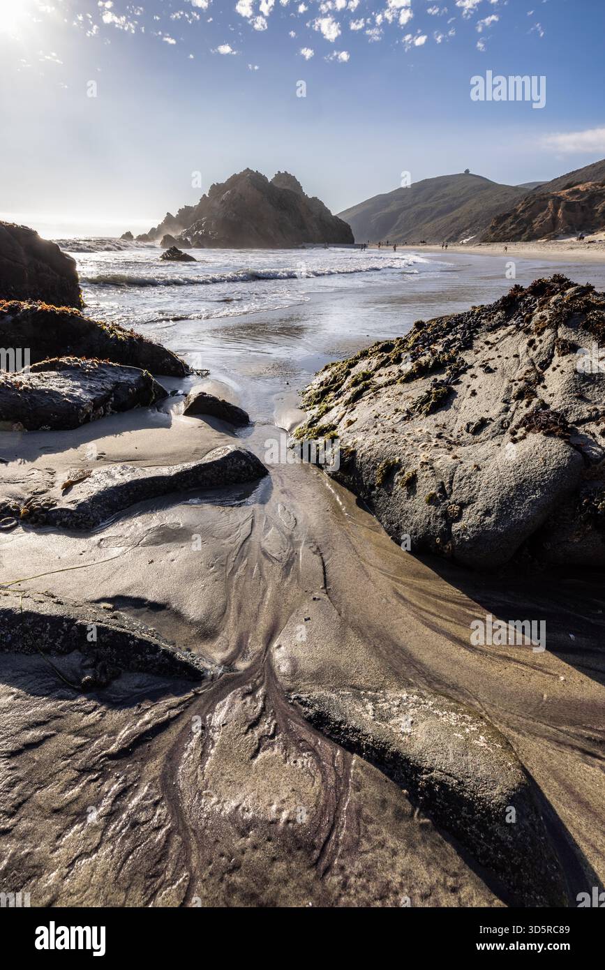 Violette Mineralsandmuster fließen zwischen den Küstenfelsen am Pfeiffer Beach, Big Sur, Kalifornien. Stockfoto